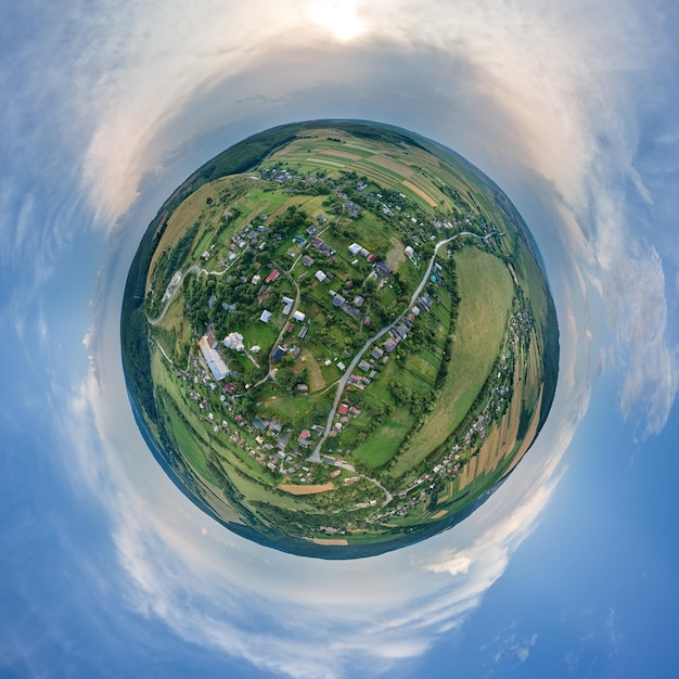 Vista aérea desde gran altura del pequeño planeta tierra con pequeñas casas de pueblo y distantes campos agrícolas verdes cultivados con cultivos en crecimiento en un brillante día de verano