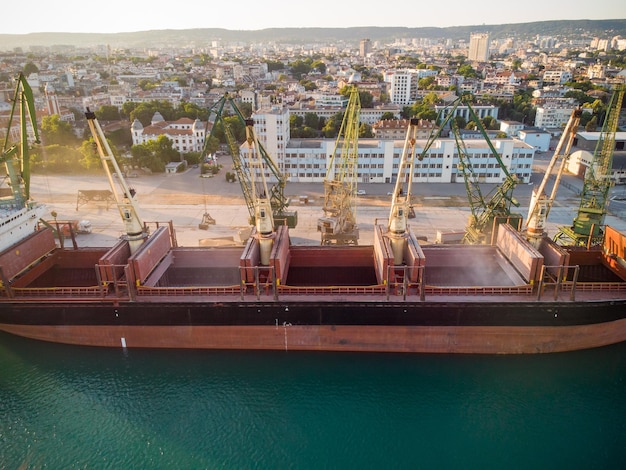La vista aérea del granelero de un gran buque de carga está cargada con grano de trigo en el puerto al atardecer