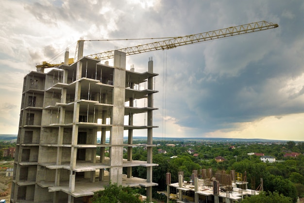 Vista aérea de la grúa de elevación de la torre y el marco de hormigón del edificio residencial de apartamentos altos en construcción en una ciudad. Desarrollo urbano y concepto de crecimiento inmobiliario.