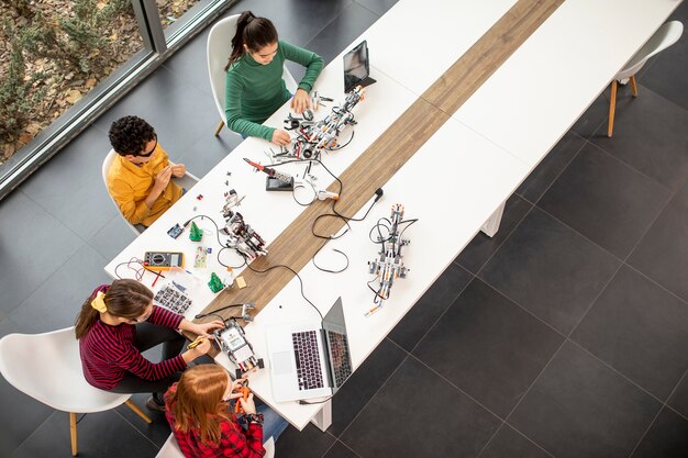 Vista aérea del grupo de niños felices que programan juguetes eléctricos y robots en el aula de robótica