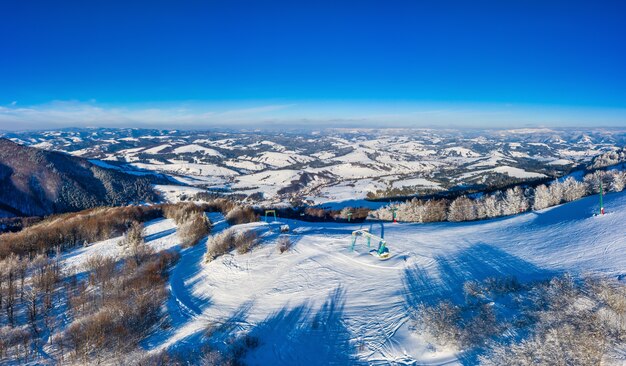 Vista aérea de las hermosas laderas de las montañas de invierno cubiertas de nieve y bosque de abetos en un día soleado y despejado. Concepto de belleza de la estación de esquí europea