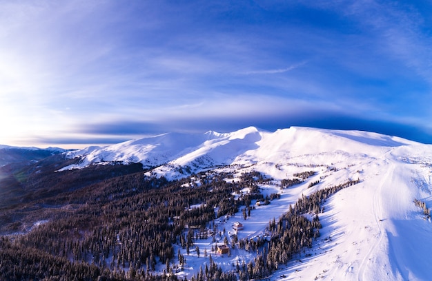 Vista aérea de un hermoso panorama brillante de una ladera de esquí con abetos y nieve en un soleado día helado con nubes humeantes