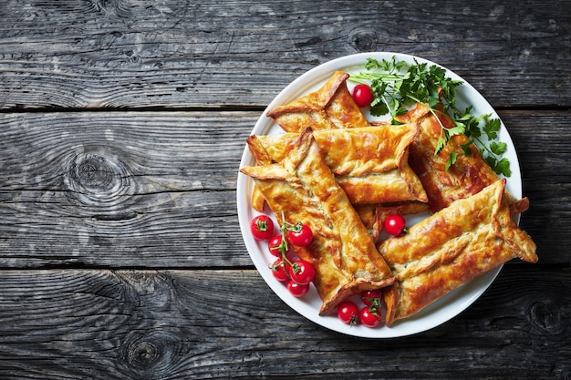 Vista aérea de hojaldre relleno de pollo Borek, pasteles de pollo al horno, paquetes de pollo hojaldre en un plato blanco con tomates cherry y perejil, vista horizontal desde arriba, espacio de copia, flatlay