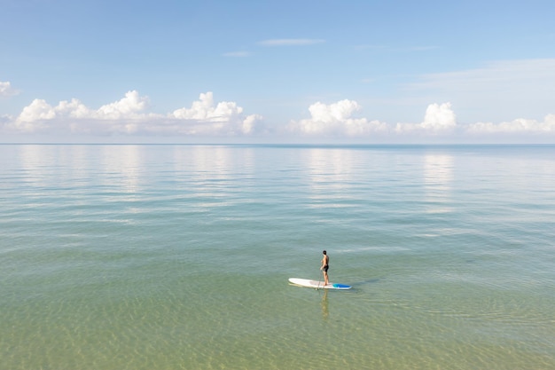 Vista aérea del hombre asiático que ejercita la tabla de sup en aguas cristalinas tropicales turquesas en día de verano.