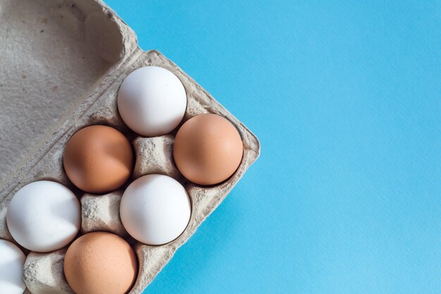 Vista aérea de huevos de gallina marrón y blanco en un cartón de huevos abierto aislado en azul claro