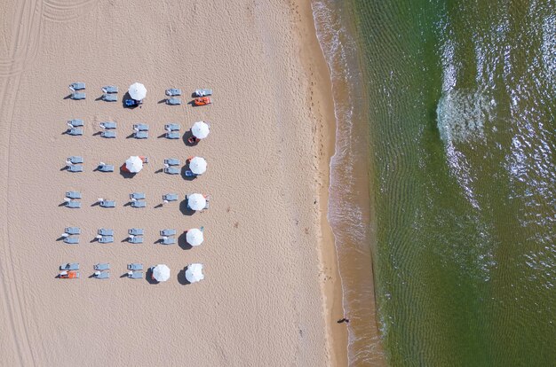 Vista aérea de una increíble playa de arena vacía con sombrillas de paja y agua turquesa clara