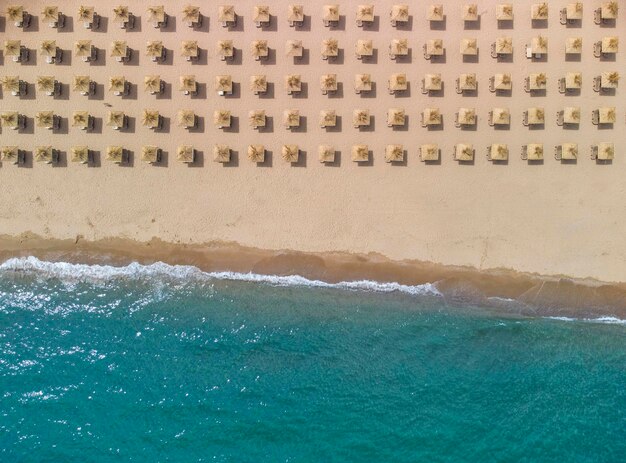 Vista aérea de una increíble playa de arena vacía con sombrillas de paja y agua turquesa clara