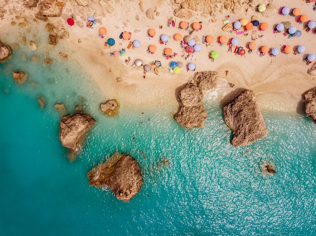 Vista aérea de la increíble playa con coloridas sombrillas y gente que se relaja y nada en aguas cristalinas del mar Mediterráneo en los días soleados.