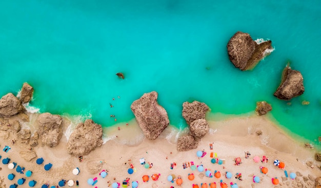 Vista aérea de la increíble playa idílica con coloridas sombrillas, tumbonas y gente que toma el sol y nada.