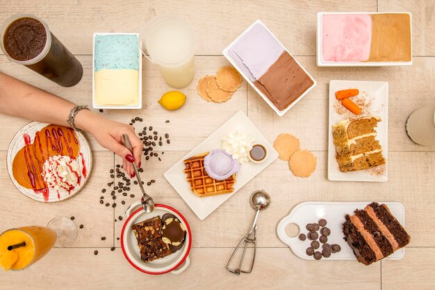 Vista aérea de un juego de platos de postre helado pastel de chocolate mano con cuchara granos de café panqueques con crema helado de sabor variado