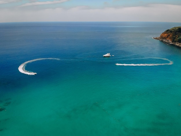 Vista aérea de la lancha rápida, dejando rastro en la superficie del mar azul cerca de la costa verde; concepto de viaje.