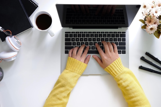 Vista aérea de manos femeninas trabajando en una moderna computadora portátil de escritorio en un escritorio blanco
