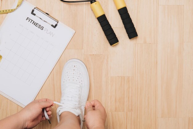 Vista aérea de las manos de la mujer atando los zapatos con equipos deportivos sobre fondo de madera