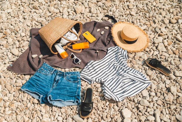 Vista aérea de la manta de cosas de playa con sombrero de paja de crema de protección solar con bolsa plana