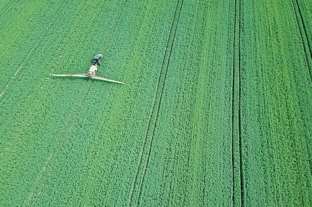 Vista aérea Maquinaria agrícola rociar productos químicos en el gran campo verde, fondo de primavera agrícola.