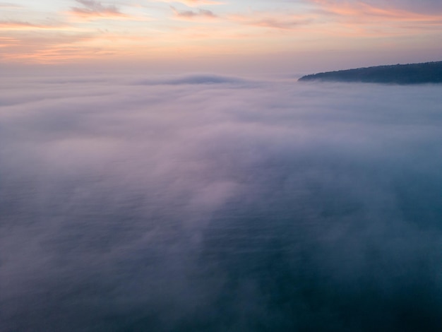 Vista aérea de un mar al amanecer con una manta de niebla matutina y rayos de sol matutinos brillando a través