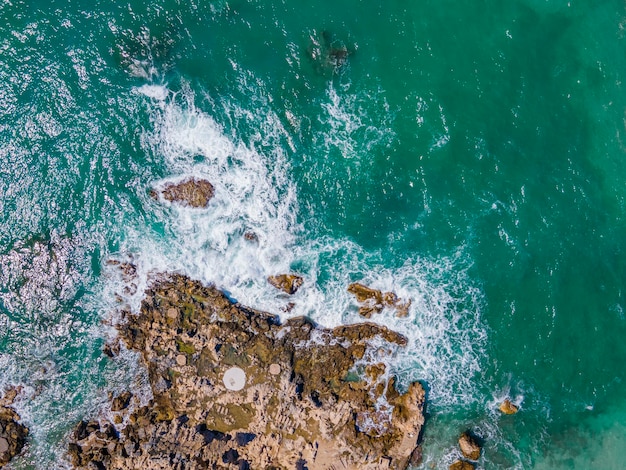 Vista aérea del mar rompiendo olas blancas olas espumosas en la vista superior de las rocas de la costa