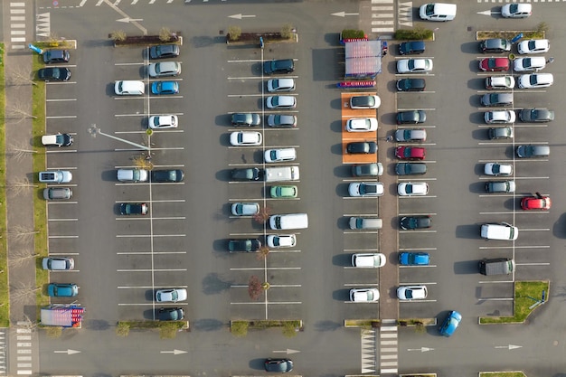 Vista aérea de muchos autos coloridos estacionados en estacionamiento con líneas y marcas para lugares de estacionamiento y direcciones