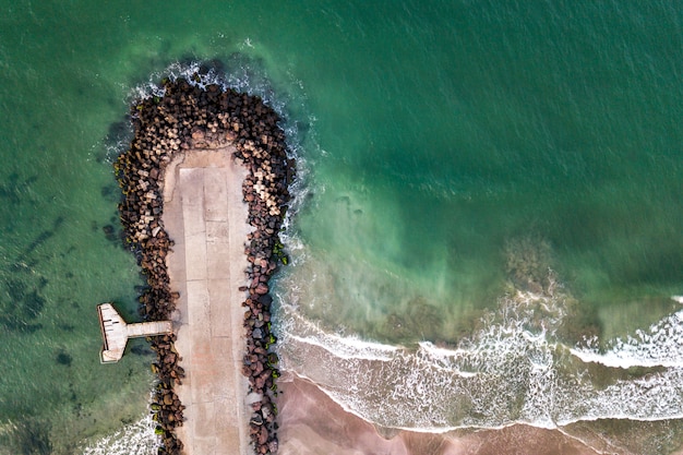 Vista aérea de un muelle de hormigón en la orilla del mar con olas rompiendo piedras.