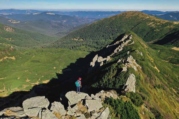 Vista aérea de mujer excursionista con mochila relajándose en la cima de una montaña y disfrutando del valle