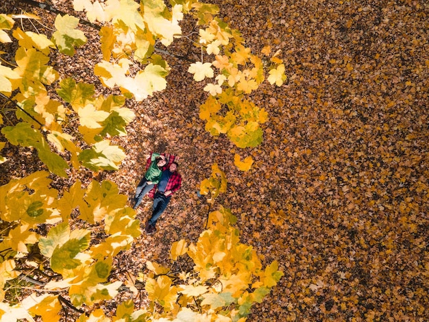 Vista aérea de la mujer con el hombre acostado en el suelo cubierto de hojas de otoño