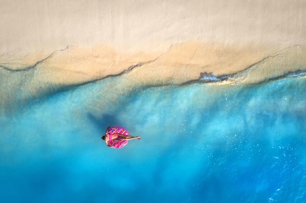 Vista aérea de una mujer joven nadando con el anillo de natación donut en el mar azul claro con olas al atardecer en verano Paisaje aéreo tropical con playa de arena de agua azul chica Vista superior Viajes