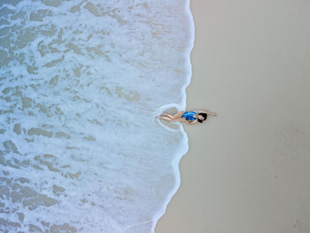 Vista aérea de la mujer en traje de baño azul en la playa del mar