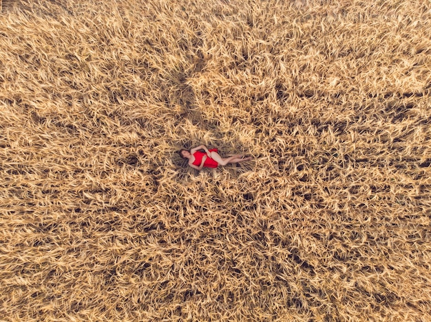 Vista aérea de la mujer en vestido rojo en el campo amarillo de trigo