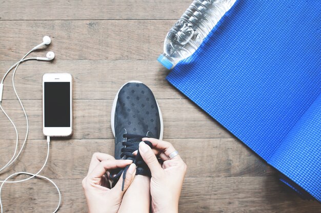 Vista aérea de la mujer en zapatillas negro con smartphone y equipo de deporte en piso de madera