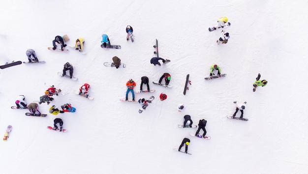 Vista aérea de una multitud de practicantes de snowboard en una pendiente nevada listos para iniciar su descenso