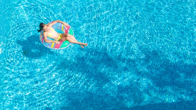 Vista aérea de la niña en la piscina desde arriba, niño nadar en anillo inflable donut y se divierte en el agua en vacaciones familiares