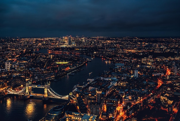 Vista aérea nocturna del Tower Bridge sobre el río Támesis con edificios iluminados que brillan en la oscuridad