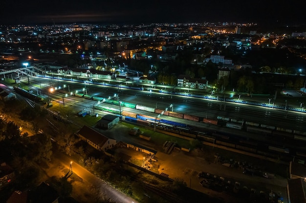 Vista aérea noturna sobre longos trens de carga ferroviários com muitos vagões parados no estacionamento