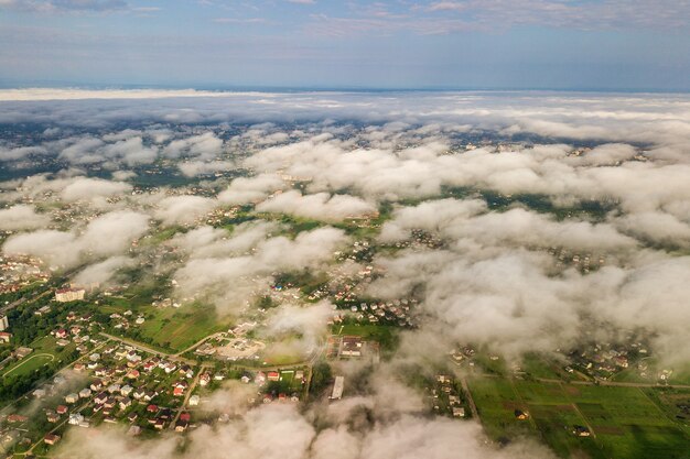 Vista aérea de nubes blancas sobre una ciudad o aldea con hileras de edificios y calles con curvas