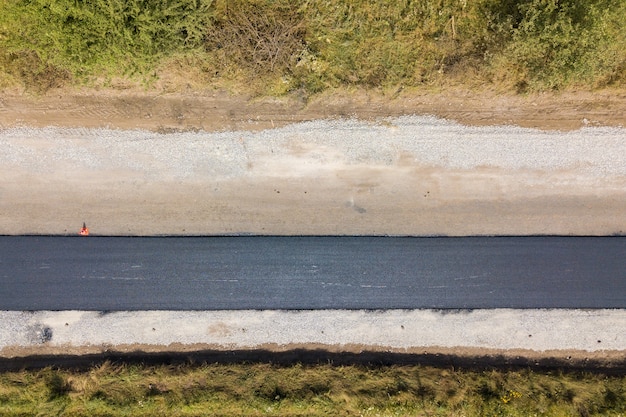 Vista aérea de la nueva construcción de carreteras con carril de asfalto negro recién colocado.