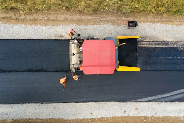 Vista aérea de la nueva construcción de carreteras con maquinaria de colocación de asfalto en el trabajo.