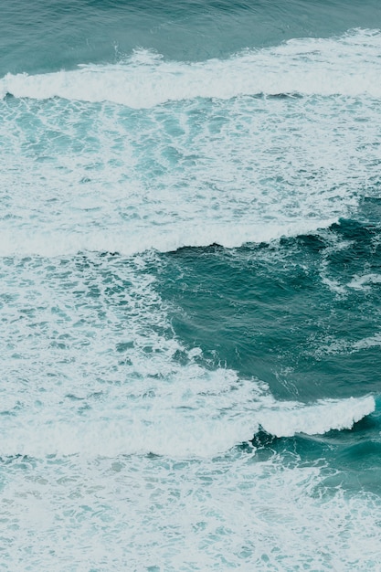 Vista aérea del océano con las olas y las rocas durante un día brillante, relajante escena en tonos azules