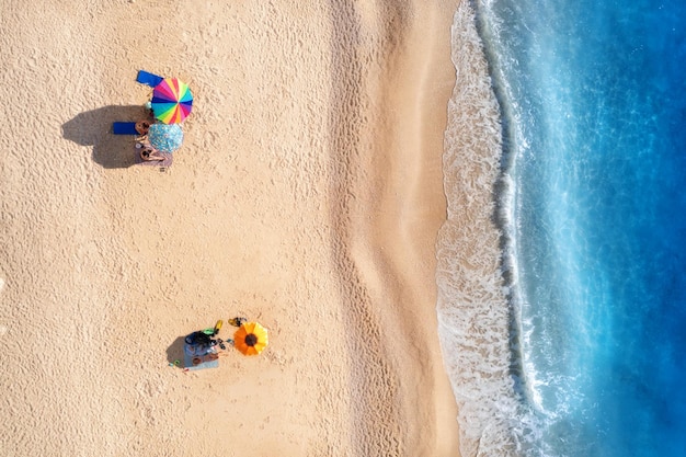 Vista aérea de las olas del mar azul, playa de arena y sombrillas con gente acostada al atardecer en verano Paisaje tropical con aguas turquesas claras Vista superior desde drones Isla de Lefkada Grecia Viajes