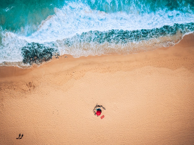 Vista aérea de las olas del mar y la playa de arena con turistas caminando - concepto de vacaciones de verano con personas - colores azul y amarillo - lugar escénico tropical con naturaleza agradable y aire libre