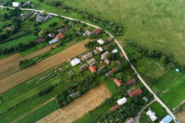 Vista aérea del paisaje de casas de pueblo y campos agrícolas cultivados verdes distantes con cultivos en crecimiento en un brillante día de verano