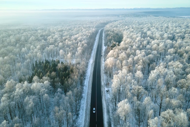 Vista aérea del paisaje invernal con bosques cubiertos de nieve y camino forestal de asfalto negro en un día invernal frío