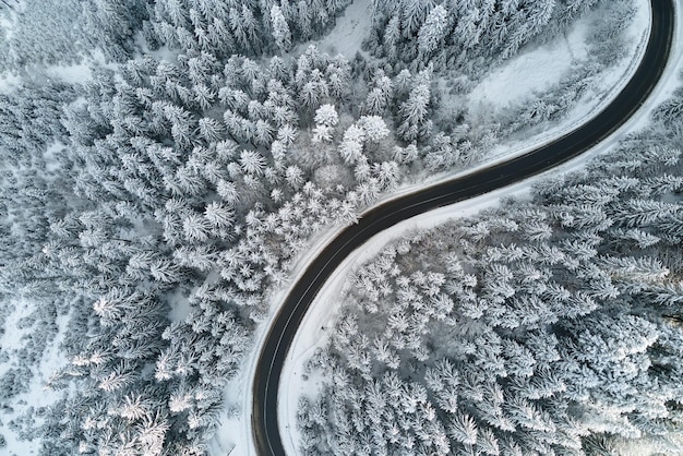 Vista aérea del paisaje invernal con bosques de montaña cubiertos de nieve y sinuoso camino resbaladizo del bosque.