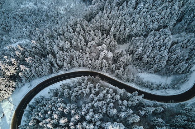 Vista aérea del paisaje invernal con colinas cubiertas de nieve y sinuoso camino forestal en la mañana.