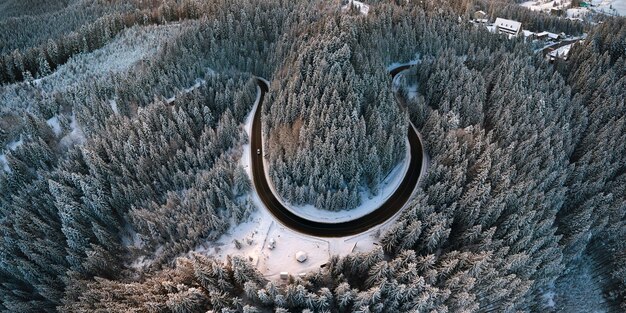 Vista aérea del paisaje invernal con colinas cubiertas de nieve y sinuoso camino forestal en la mañana.