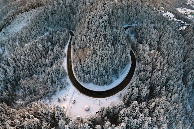 Vista aérea del paisaje invernal con colinas cubiertas de nieve y sinuoso camino forestal en la mañana.