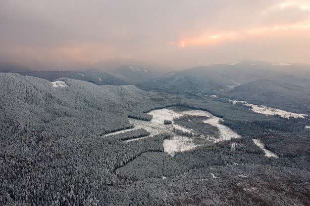 Vista aérea del paisaje invernal con colinas cubiertas de pinos de hoja perenne después de fuertes nevadas en la fría noche tranquila.