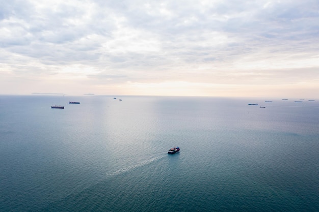 Vista aérea del paisaje marino y un pequeño buque portacontenedores flotando en el horizonte marino y el fondo del cielo nuboso en