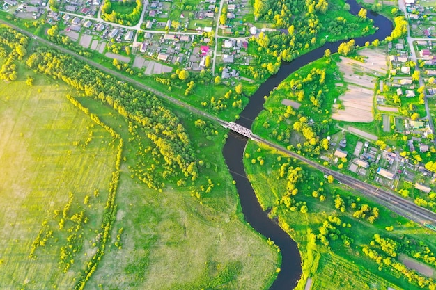 Vista aérea del paisaje de un pequeño río sinuoso entre el pequeño arroyo de la ciudad en la vista superior del prado de campo verde