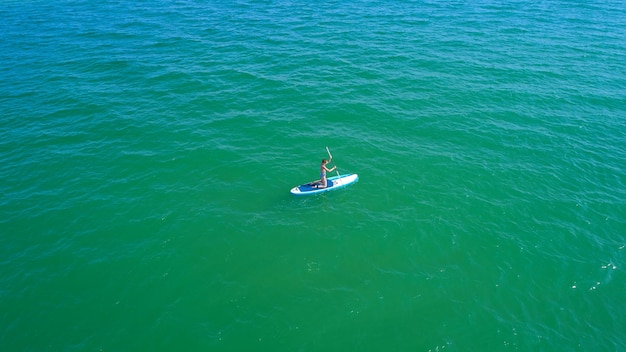 Vista aérea de pájaros no tripulados de una mujer joven que ejercita sup en aguas turquesas tropicales claras