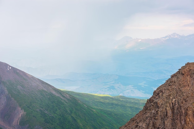 Vista aérea panorámica desde rocas altas y afiladas hasta colinas verdes y una cordillera iluminada por el sol en nubes lluviosas durante la lluvia Paisaje dramático con inmensidad montañosa a la luz del sol en nubes en un clima cambiante